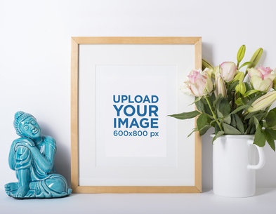 Mockup of a Photo Frame Standing Against a White Wall and Next to Some Flowers 593-el